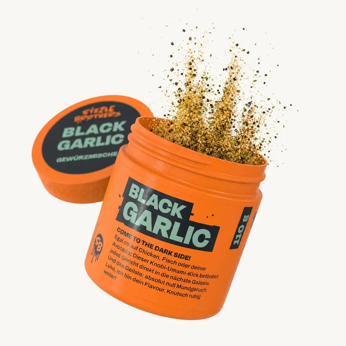 Oranger Behälter mit Text "BLACK GARLIC", Gewürzpulver spritzt heraus.