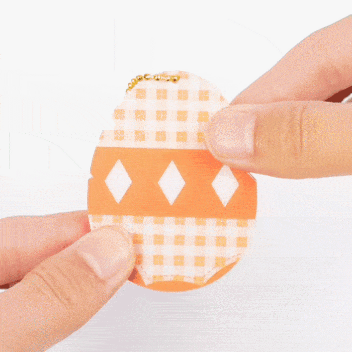 Hands sliding open a custom acrylic puzzle charm with orange and white checkered design and gold chain