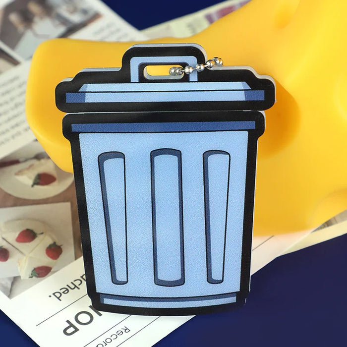 Custom acrylic keychain shaped like a blue trash can with a metallic chain, on papers