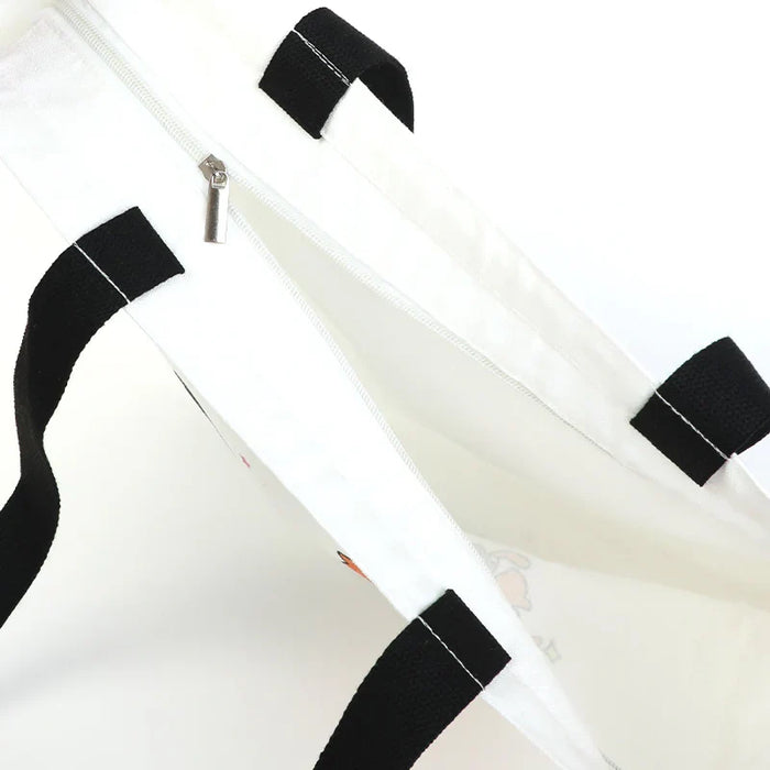 White tote bag with black handles and zipper, featuring subtle cartoon print for anime merch