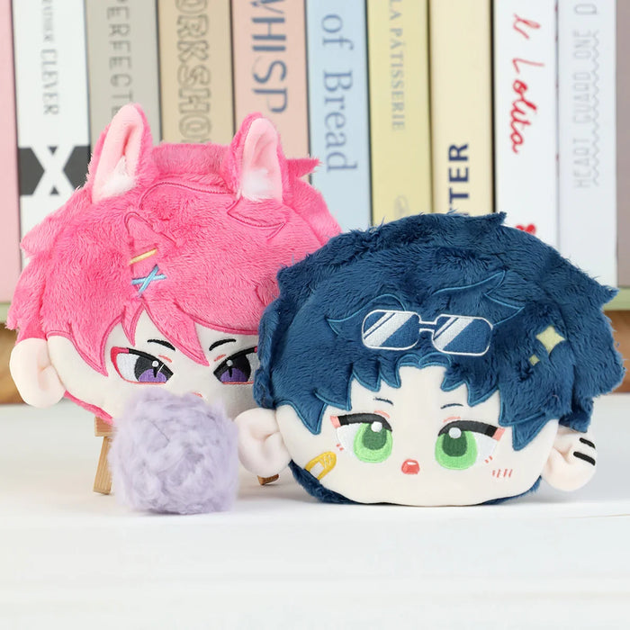 Two cute anime-style plush pillows with pink and blue hair, cartoon faces, on a desk.