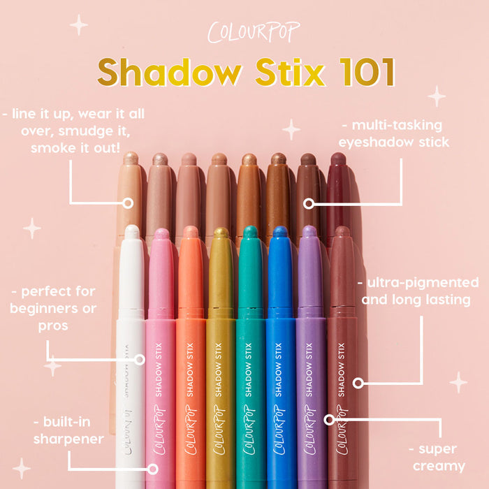 Juicy Gossip Shadow Stix stands upright among a rainbow lineup of ColourPop Shadow Stix, caps off to show creamy tips on a pink backdrop; ultra‑pigmented, long‑wear, multi‑tasking eyeshadow stick with a built‑in sharpener.