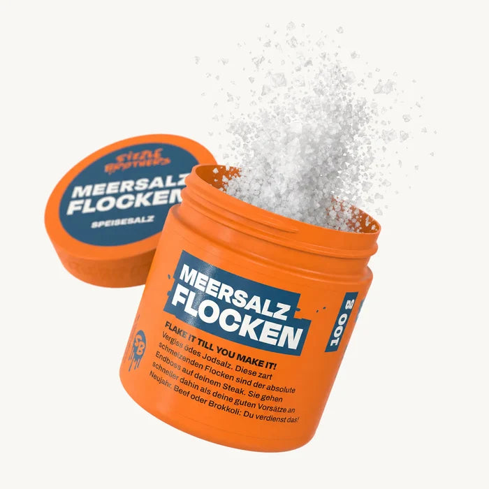 Orangene Dose mit Aufschrift 'MEERSALZ FLOCKEN', weißes Salz flockt heraus.