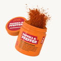 Orangene Dose mit Aufschrift 'PAPRIKA & PFEFFER', rotes Gewürz flockt heraus.